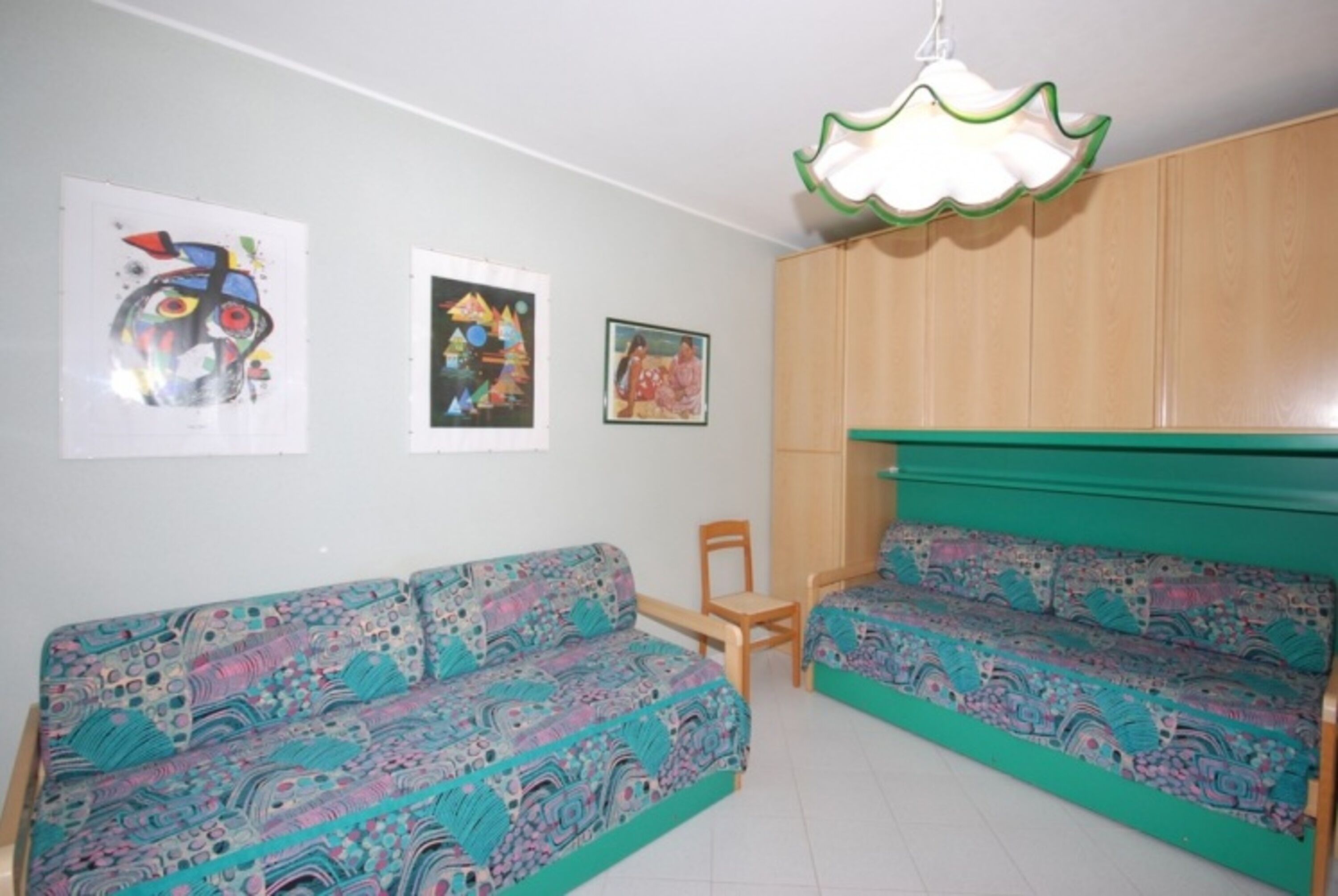 A room with two patterned sofas, a wooden chair, and artwork on the walls.