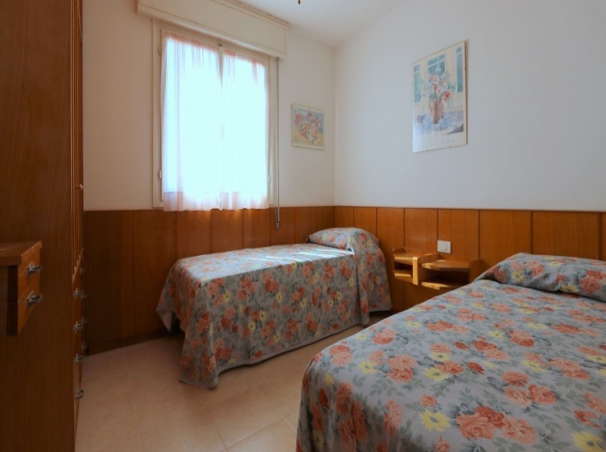 Une chambre avec deux lits, des lambris en bois, une fenêtre avec des rideaux et un tableau au mur.