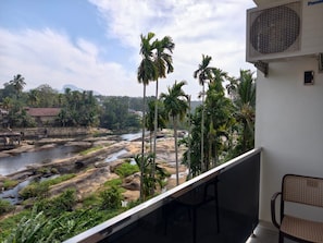 A balcony with a view of a river and palm trees, a chair, and an air conditioning unit. - Falls Regency (Vilavancode)