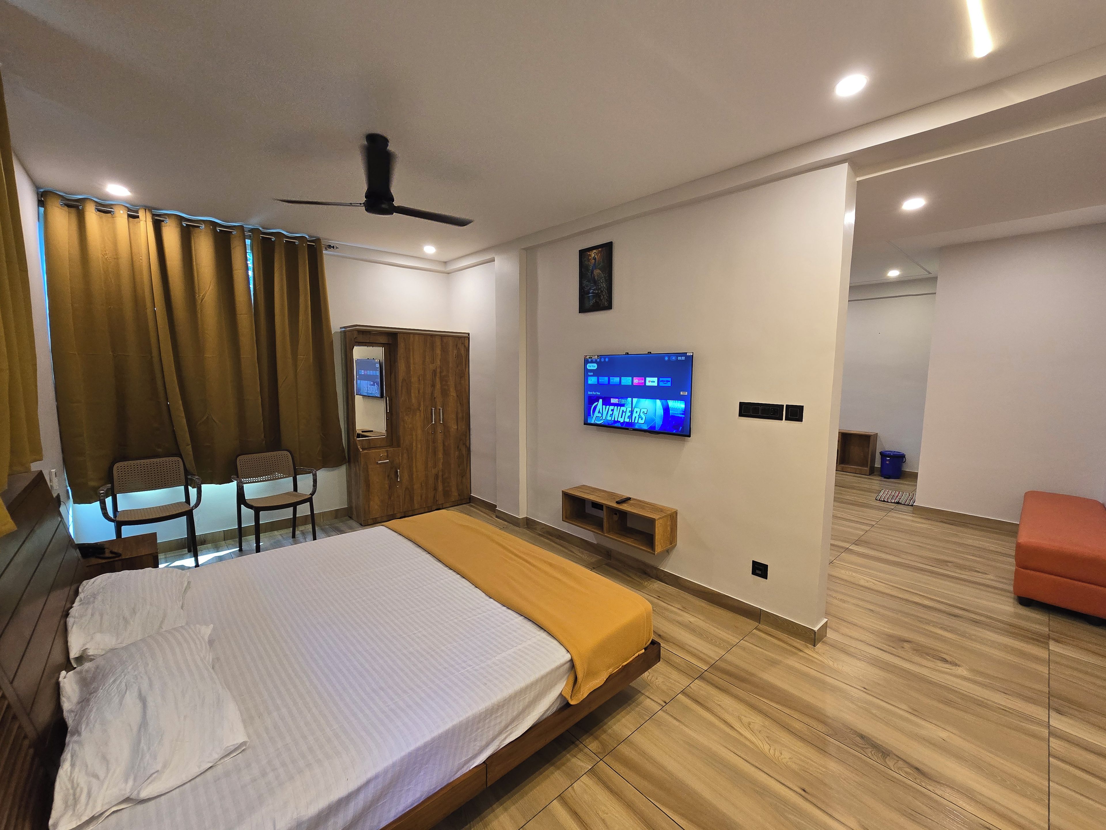 Una habitación de hotel moderna con una cama, un televisor montado en la pared, un ventilador de techo y piso de madera.
