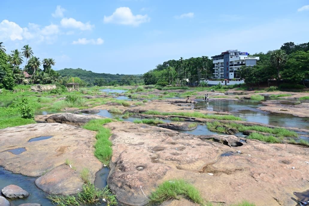 A natural landscape with a rocky terrain, water bodies, and a building in the background.