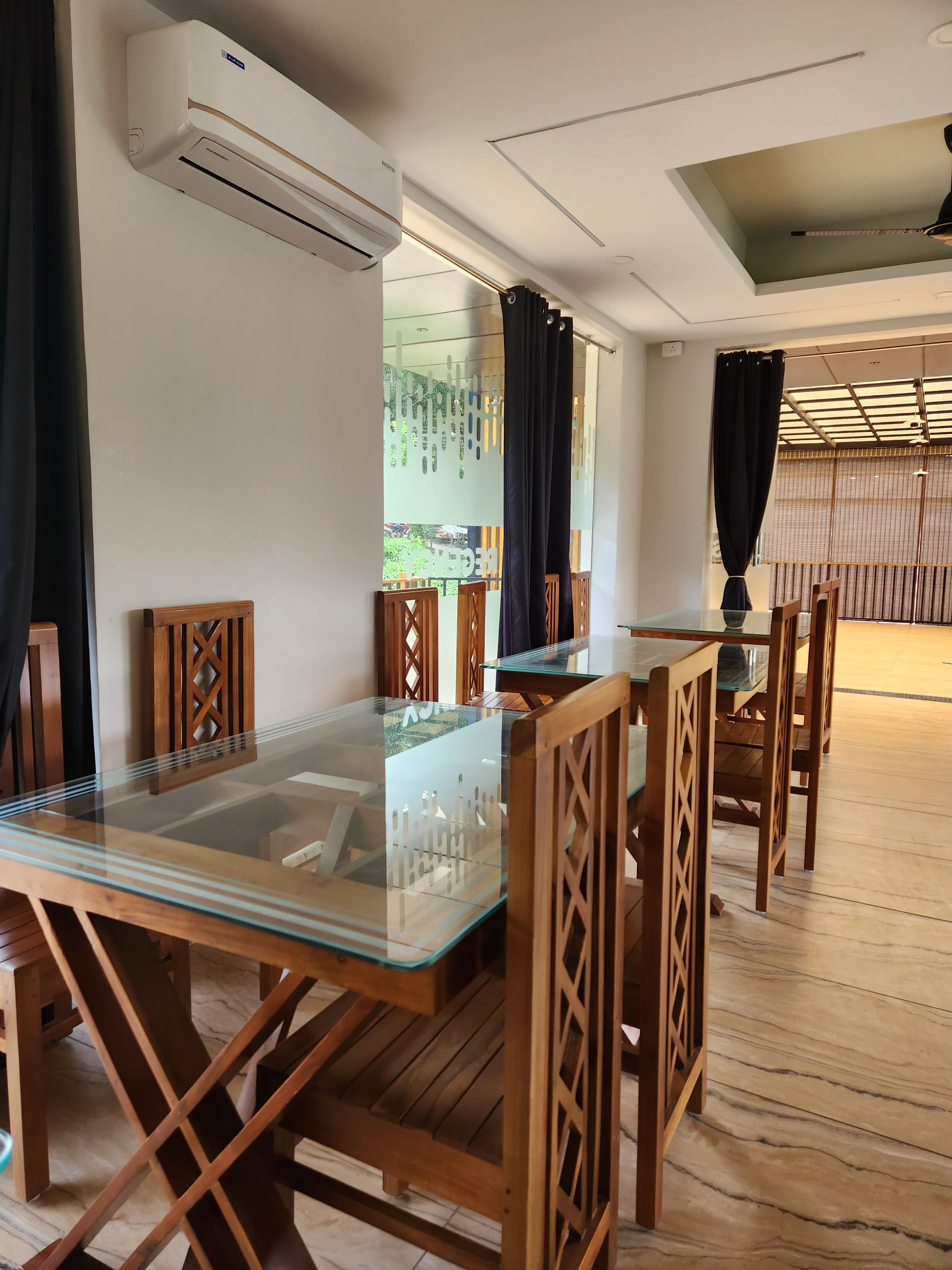 Uma sala de jantar com mesa de vidro, cadeiras de madeira e ar condicionado na parede.