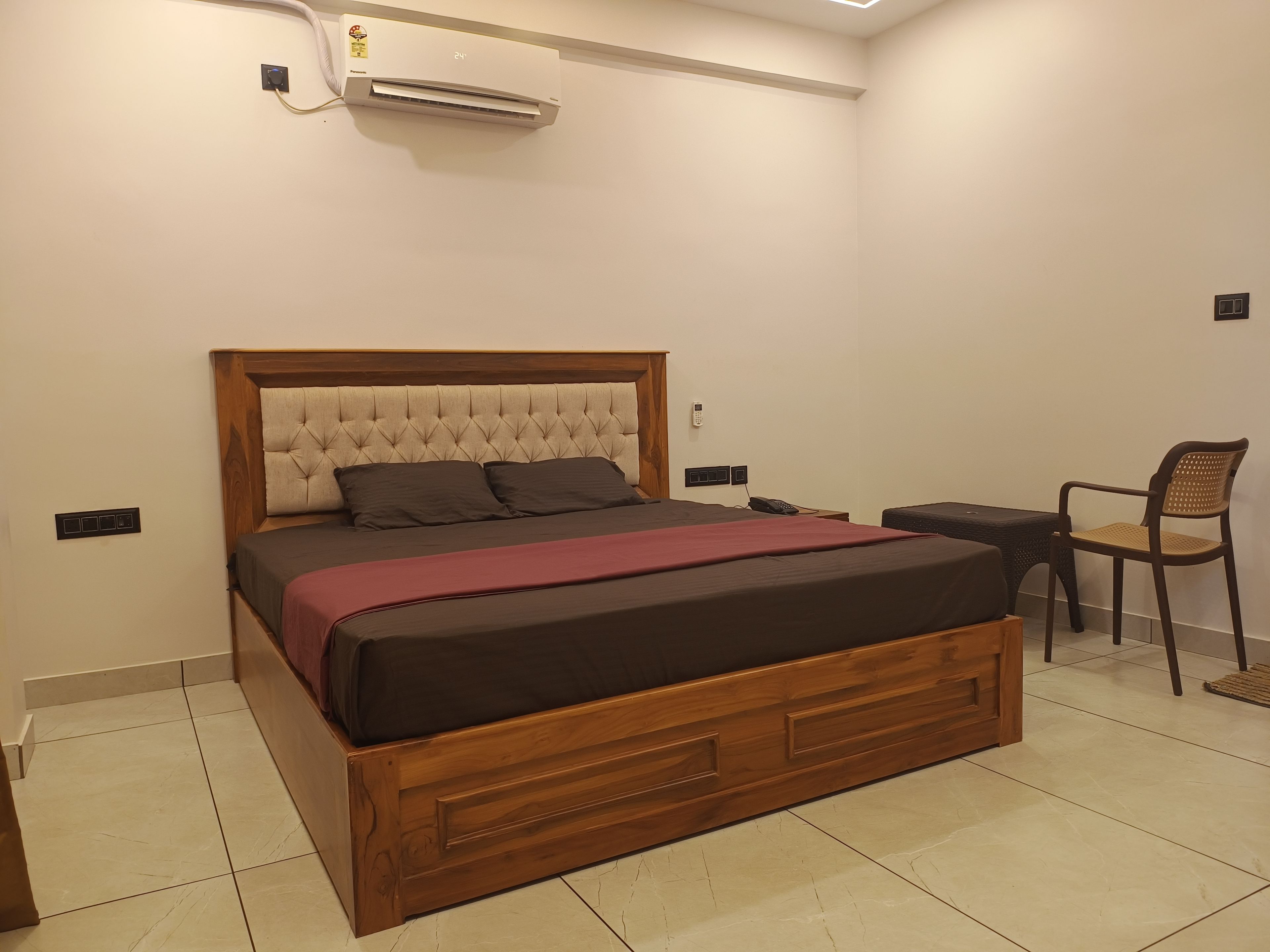 Un dormitorio con una cama de madera, una mesita de noche, una silla y un equipo de aire acondicionado.