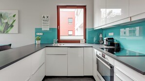 Une cuisine moderne avec des meubles blancs, un plan de travail noir, une fenêtre avec des stores et une plante en pot.