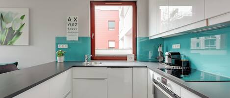 A modern kitchen with white cabinets, a black countertop, a window with blinds, and a potted plant.