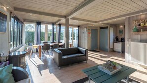 Amplia sala de estar con sofá, mesa de comedor y sillas, zona de cocina con electrodomésticos y ventanas amplias que ofrecen vistas al exterior.