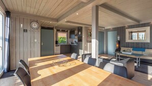 Un comedor espacioso con una larga mesa de madera y sillas modernas, una cocina al fondo, y una zona de estar acogedora con un sofá y una mesa de centro.