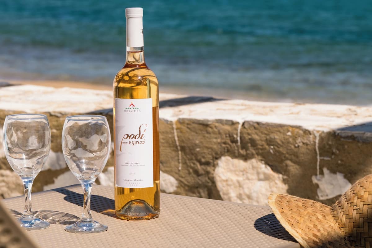 A bottle of wine and two glasses on a table by the sea.