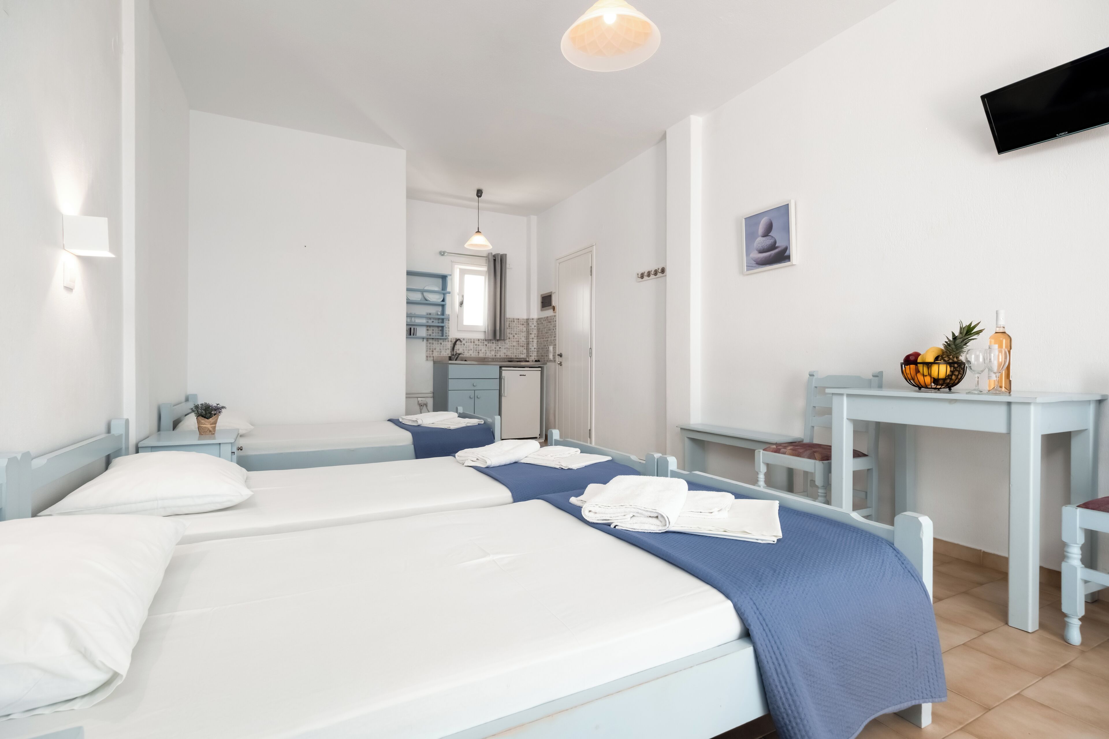 Habitación de hotel con dos camas, un escritorio, una silla, un televisor y una pequeña cocina.