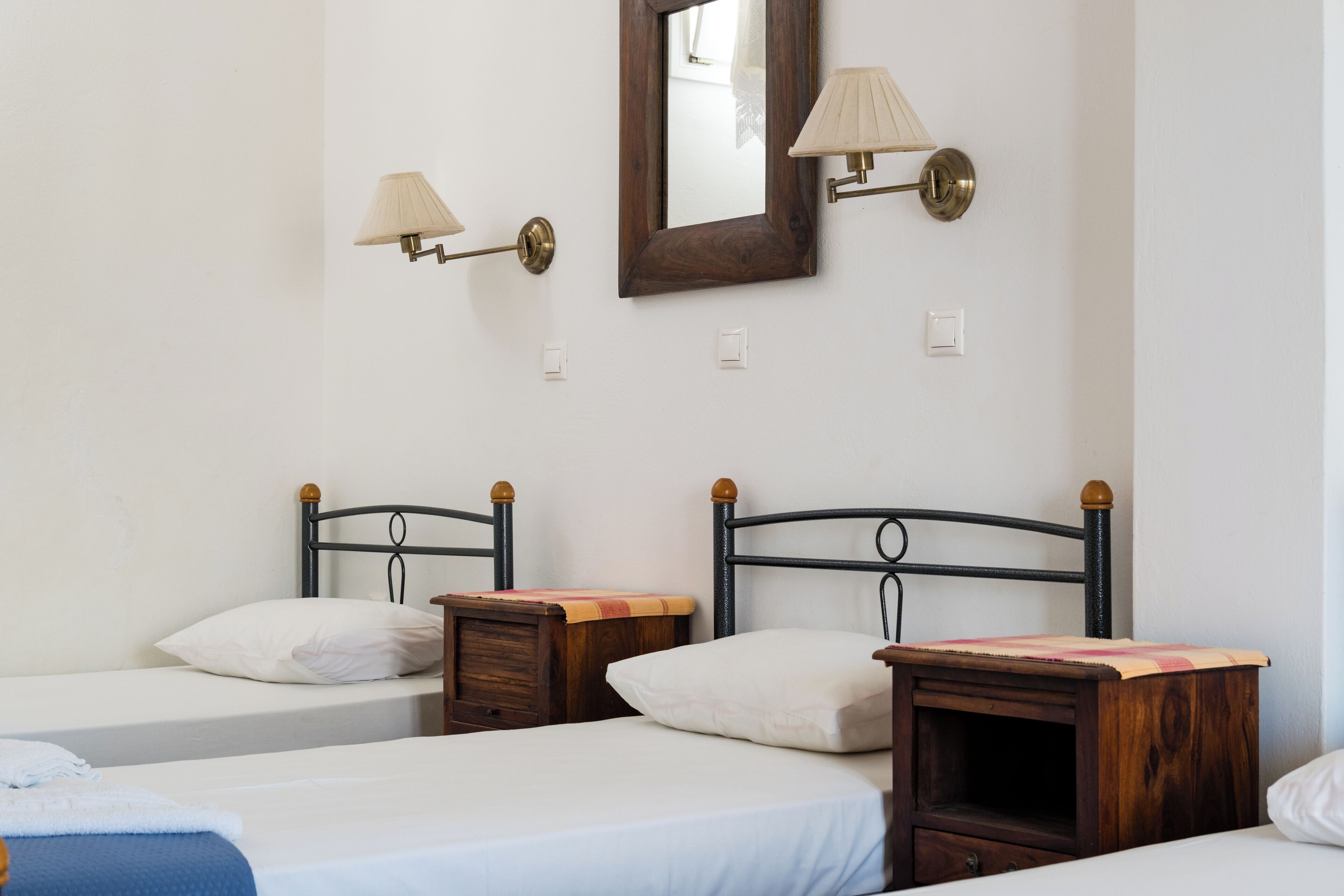 Quarto com duas camas, mesas de cabeceira de madeira e luminárias fixadas na parede.