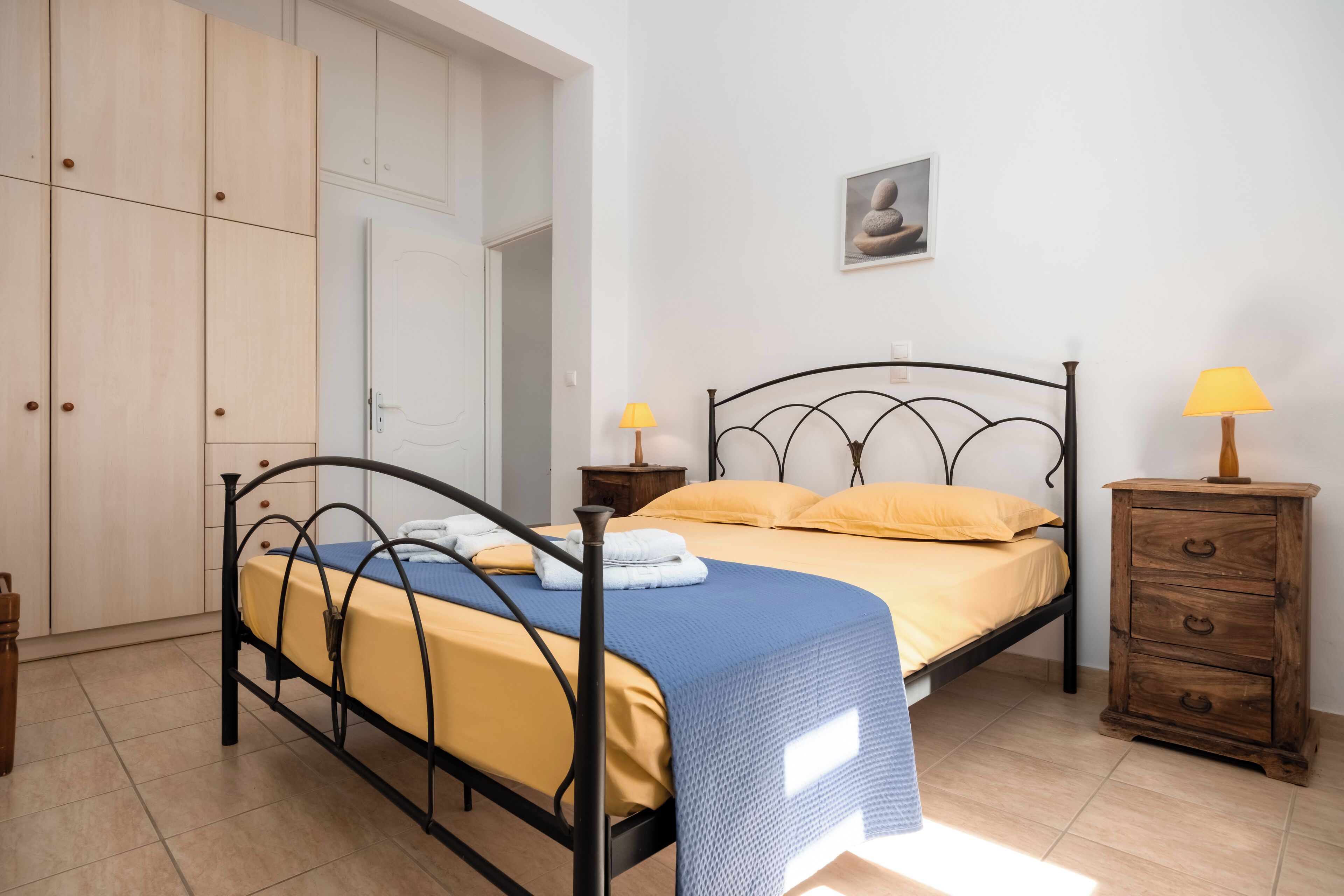 A bedroom with a bed, wooden wardrobe, bedside tables, and a wall-mounted picture.