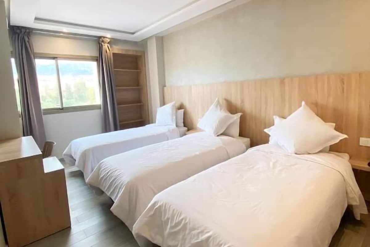 Habitación de hotel con dos camas, cabecera de madera, escritorio y ventana con cortinas.