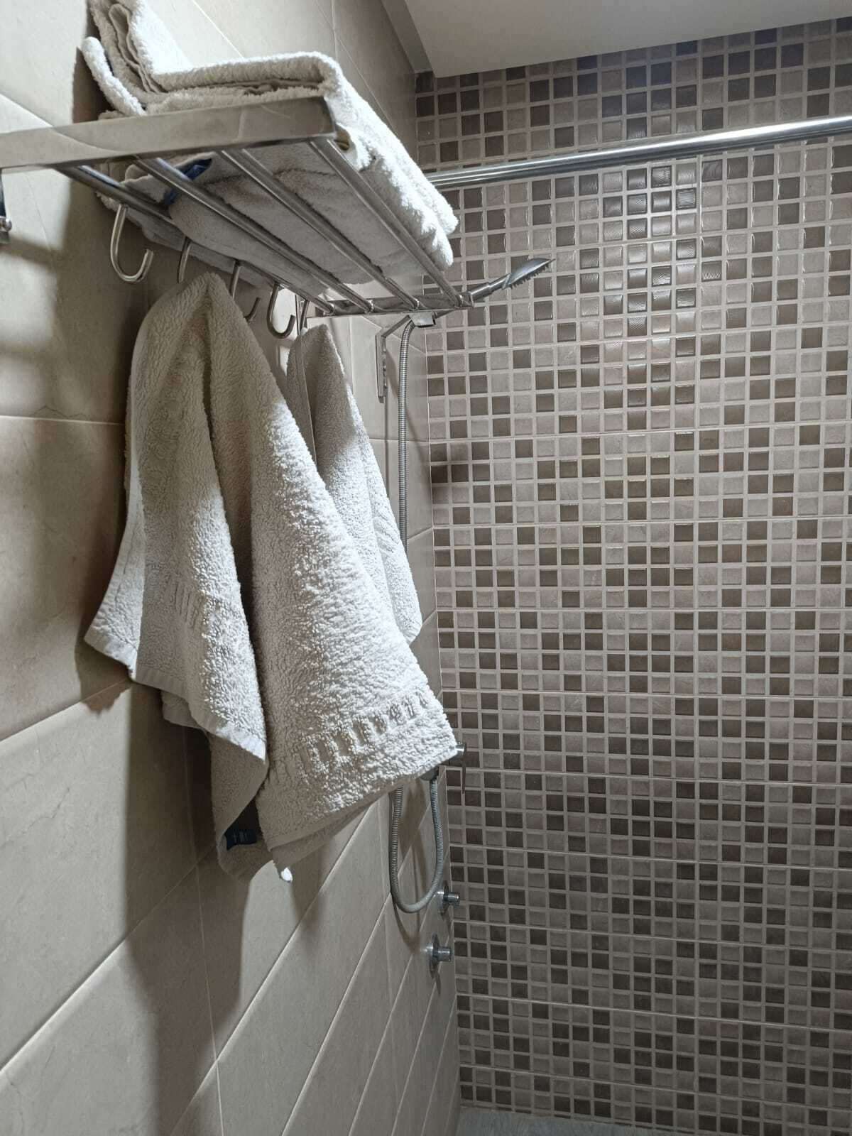 A bathroom with a tiled shower wall, a towel rack with folded towels, and a showerhead.