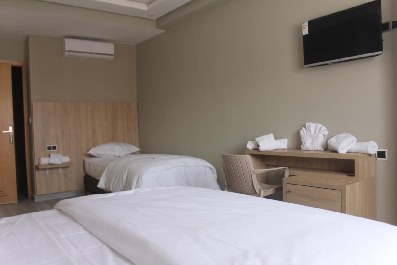Een hotelkamer met twee bedden, een aan de muur bevestigde televisie, een houten hoofdeinde, een bureau met stoel en een plank met handdoeken.