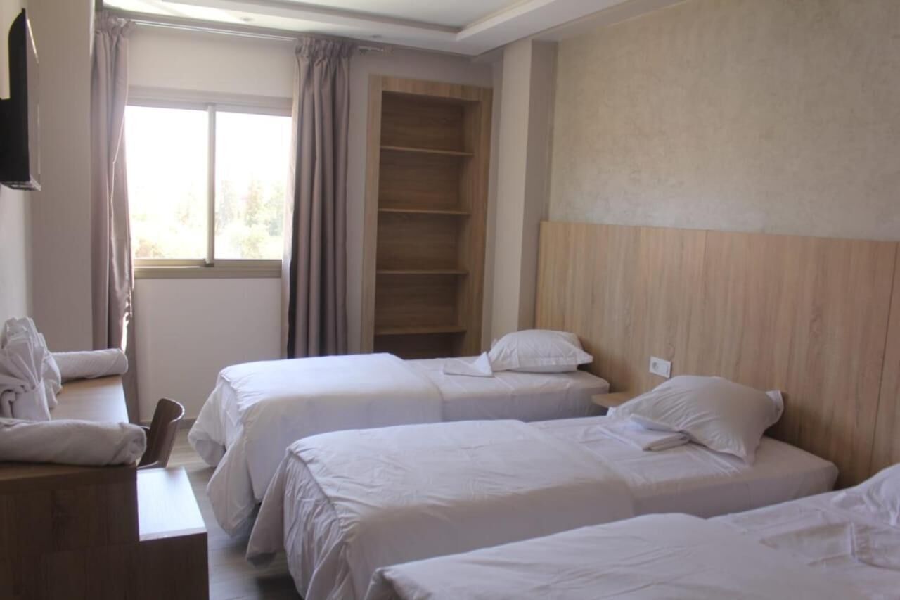 A hotel room with two beds, a wooden headboard, a wardrobe, and a window with curtains.