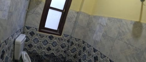 A bathroom with a toilet, a window, a shower, and a sink.
