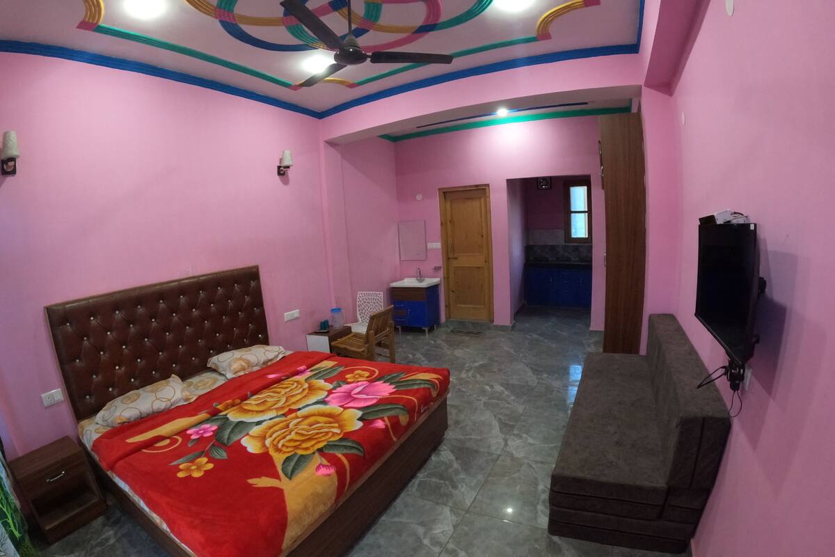 A bedroom with a bed, a TV, a ceiling fan, and a bathroom visible in the background.