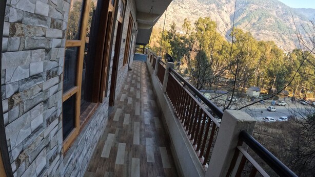 Un couloir aux murs de pierre et au plancher en bois mène à un balcon doté d’une rambarde en métal.
