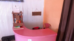 Un comptoir d’accueil rose, doté d’une petite étagère où sont posés des livres et d’une pancarte.