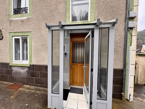 A small, enclosed entryway with a wooden door and a glass door, leading to a tiled entrance area. - Les Capucines Le Mont Dore 2pers (Mont-Dore)