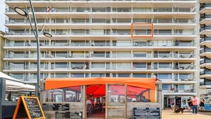 En byggnad med flera våningar och balkonger, en restaurang med ett orangefärgat markis och en skylt med rätter från menyn.