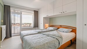 Ett sovrum med två sängar, ett stort fönster med gardiner, ett element och en garderob.