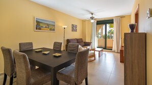 Un coin repas avec une table en bois foncé et six chaises, un canapé et un ventilateur de plafond.