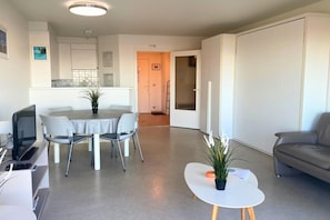 A modern living room with a dining area, a sofa, a TV, and a small table with a plant.
