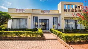 A modern two-story building with a symmetrical facade, large windows, and a well-maintained garden with hedges and a pathway leading to the entrance. - TB 11 (Kibaoni)