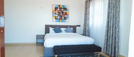 A bedroom with a bed, a bench, a nightstand, a patterned rug, and a painting on the wall.