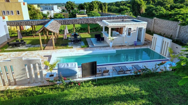 A swimming pool with lounge chairs, a covered seating area, and a small pavilion. - TB 11 (Kibaoni)