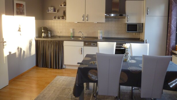 A compact kitchen with white cabinets, a microwave, and a stove. There is a dining table with chairs and a small rug. - Vacation apartment Luna (Aurich)
