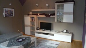 A living room with a sofa, coffee table, TV stand, and shelves. - Vacation apartment Luna (Aurich)