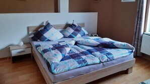 A bedroom with a wooden bed, a nightstand, a bedside table, and a wall-mounted heater. - Vacation apartment Luna (Aurich)