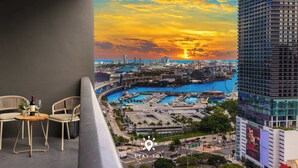 A balcony with two chairs and a table, overlooking a marina with boats and a sunset. - 1BR Apartment - Pool & Gym (Miami)