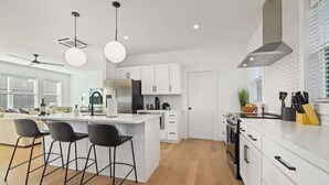 Une cuisine moderne avec des meubles blancs, un îlot central doté de tabourets et une grande fenêtre qui laisse entrer la lumière naturelle.