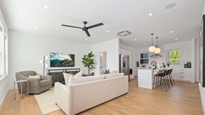 Un vaste espace de vie comprenant un canapé, un fauteuil et un coin repas avec des tabourets de bar.