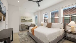 Um quarto moderno com uma cama grande, duas mesas de cabeceira com abajures, um ventilador de teto e um quadro na parede.