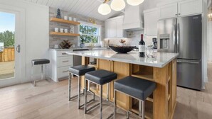 Une cuisine moderne dotée d’un grand îlot central, d’appareils électroménagers en acier inoxydable et offrant une vue sur l’extérieur.