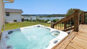 Un bain à remous sur une terrasse en bois, avec vue sur un lac et des collines en arrière-plan.