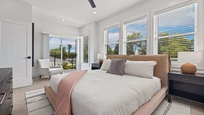 A modern bedroom with a large bed, two bedside tables, a ceiling fan, and large windows with blinds.