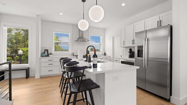 A modern kitchen with white cabinetry, a stainless steel refrigerator, and a central island with bar stools.