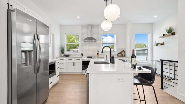 A modern kitchen with white cabinetry, a stainless steel refrigerator, a central island with bar stools, and pendant lighting.
