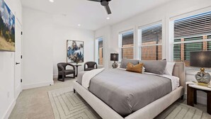 Un dormitorio moderno con una cama grande, un ventilador de techo y vistas a la ciudad a través de las ventanas.