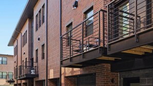 Un edificio moderno de varios pisos con paredes exteriores de ladrillo, ventanas grandes y un espacio exterior cubierto con barandilla de metal.