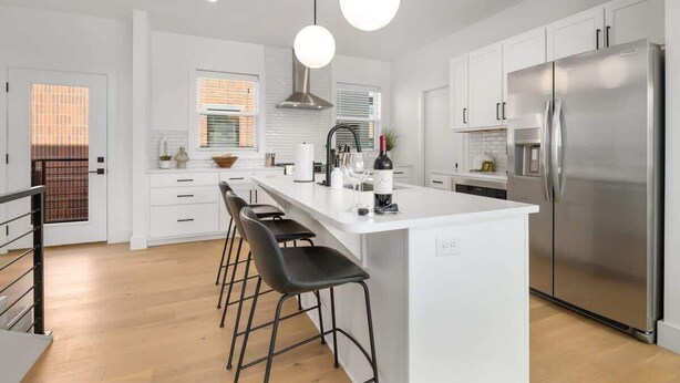 Una cocina moderna con una isla central, electrodomésticos de acero inoxidable y taburetes negros.