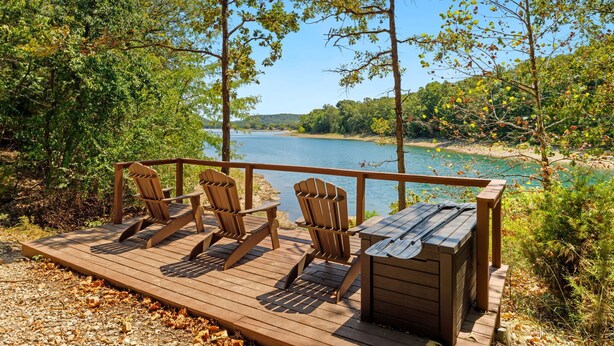 Eine Holzterrasse mit Adirondack-Stühlen und einem kleinen Tisch mit Blick auf einen See.
