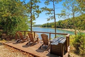Une terrasse en bois avec des fauteuils Adirondack et une petite table, le tout offrant une vue sur un lac.