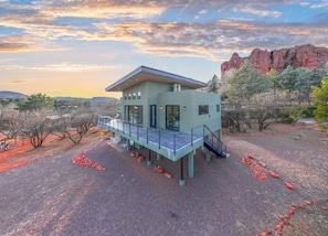 A modern house with a balcony, surrounded by a dry landscape and a mountain in the background.