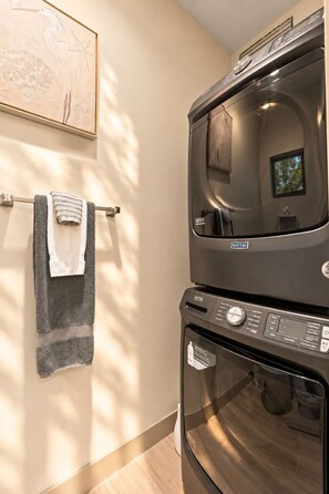 Une salle de bain moderne avec une laveuse et une sécheuse Maytag superposées, un porte-serviettes avec des serviettes et une œuvre d’art encadrée accrochée au mur.